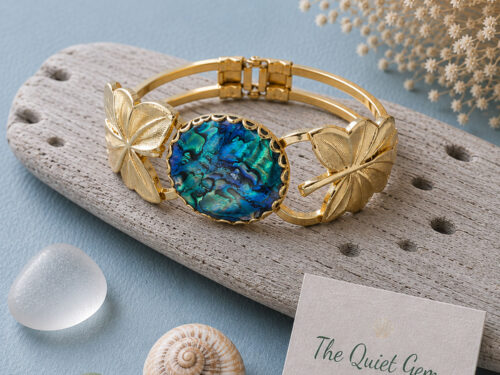 Vintage gold tone hinged clamper cuff bracelet with a vibrant blue abalone shell centerpiece, detailed maple leaf accents, and double gold bands displayed on a white background.