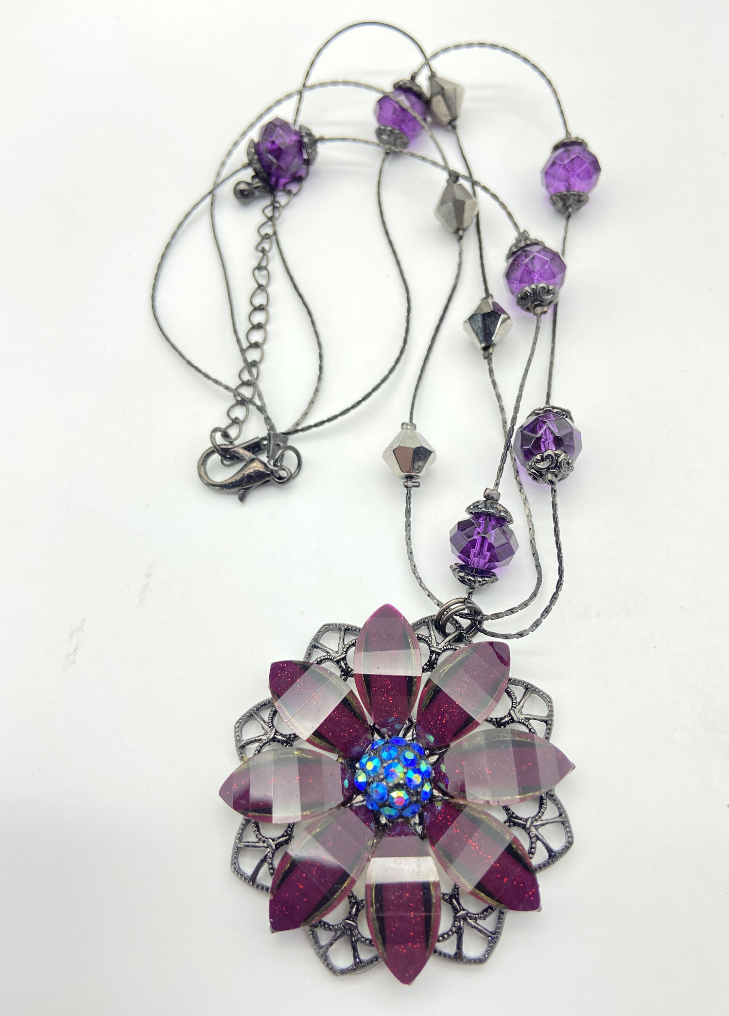 Purple Lucite flower pendant necklace with glittery petals, a faceted iridescent AB bead centre, purple accent beads, and a double-strand black chain.