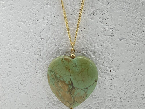 Close-up of one side of a reversible dyed green magnesite heart pendant with earthy veining and gold-tone necklace chain.