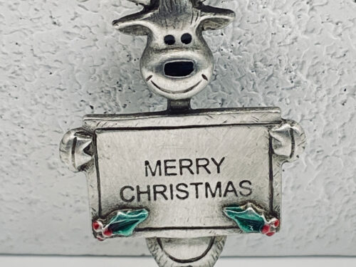 Vintage pewter-tone reindeer brooch holding a Merry Christmas sign with green holly leaves and red berries.